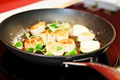 Scallops with field thyme, sea salt and butter being fried in a pan