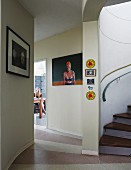 Bilder an getönter Wand im Vorraum, seitlich teilweise sichtbare Wendeltreppe, im Hintergrund offene Tür und Blick auf junge Frau