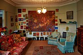 Sofa in vintage floral pattern and pale blue armchairs in artistic interior; large painting surrounded by many small paintings on wall
