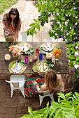 Two women sitting at set garden table below flowering shrub in summery garden party atmosphere