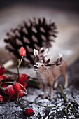 Toy stag, rose hips, pine cone and artificial snow on wooden table