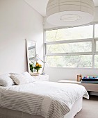 Helles, weißes Schlafzimmer mit breitem Fensterband und angelehntem Wandspiegel auf Nachtkästchen