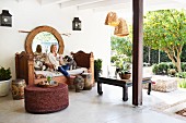 Relaxing on a veranda; woman and dogs on antique bench, rattan pouffe and view into garden to one side
