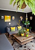 Pflanzengefässe auf rustikalem Coffeetable, Tierfellteppich auf Boden, dahinter Sitzbänke mit Polstern vor schwarzer Wand