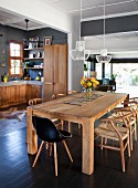 Schwarzer Schalenstuhl und Stühle im Klassikerstil um Massivholztisch im Wohnraum mit offener Küche