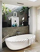 Free-standing designer bathtub against grey facing formwork with wall-mounted taps in contemporary bathroom with pattern of light and shadow on wall