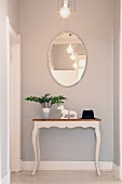 Oval mirror above dachshund bookends on vintage console table at end of hallway