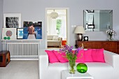 White sofa with row of hot pink scatter cushions behind vase of flowers on side table