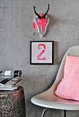 In Neon-Pink bemalter Geweihschädel auf mit Blattsilber belegter Holzplatte und Typo-Bild an Betonwand