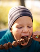 A child eating a meatball skewer at an autumn picnic