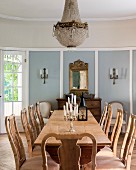 Long rustic wooden table and chairs with carved backrests in dining room of elegant country house with candlesticks on table and candle sconces
