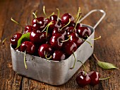 Freshly washed cherries in a metal container on a wooden surface
