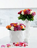 Bunte Rosensträusse in weisser Porzellanvase mit rautenförmiger Struktur und verstreute Blütenblätter auf weißem Untergrund