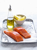 Salmon fillets on ice with olive oil and lemon wedges
