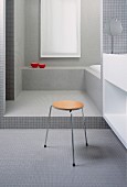 Modernes Badezimmer mit Mosaikfliesen, Dreibeinhocker vor Waschtisch im Vordergrund