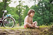 Mädchen im Schneidersitz am Wegesrand; im Hintergrund ein Fahrrad