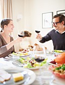 A couple raising a toast with glasses of red wine at a table laid for Thanksgiving