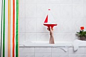 Menschliche Hand ragt aus Badewanne & hält ein Spielzeugboot