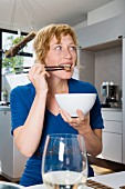 A woman eating a stir-fry with chopsticks in a kitchen