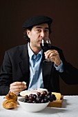 A stereotypical French man drinking red wine with a cheese platter