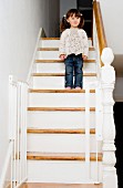 Kleines Mädchen auf Holztreppe, im Vordergrund offene Gittertür