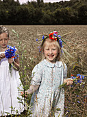 Two girls in a wheat field with bunches of wildflowers