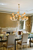 Elegant dining room with fireplace and illuminated chandelier above long glass table in historical, English manor house