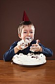 A boy smeared with cream eating cake with his hands