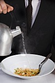 Ein Mann gießt Wasser auf Instant-Suppenpulver in einer Schüssel