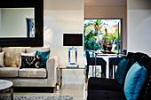 Modernes Wohnzimmer mit Sofas, Wandspiegel, Metalltisch, Teppich und Beistelltischchen aus Glas mit Lampe