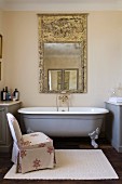 Nostalgic bathtub and loose-covered easy chair below artistic mirror on wall