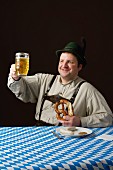 A stereotypical German man wearing lederhosen and eating a pretzel and white sausage with beer