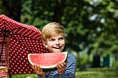A young boy holding a slice of watermelon at a picnic