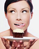 A woman holding a cupcake on a plate and licking her lips