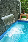 Waterfall emerging from screen of stacked stones next to pool