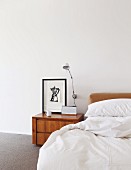 Wooden bedside cabinet and wall-mounted lamp next to bed with white bed linen