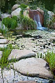Pond with aquatic plants, large stone slabs and waterfall