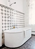 White, free-standing bathtub on terrazzo floor against wall tiled in black and white vintage pattern