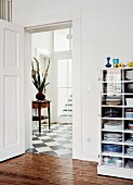 Half-height, glass-fronted cabinet painted white next to open door with view into foyer with chequered floor