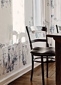 Antiker Holzstuhl mit Schnitzereien auf der Lehne und graues Sitzkissen, vor Wand mit minimalistischer Bemalung