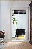Free-standing bathtub with black outside and gold stripe seen through open door