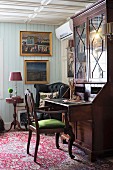 Antique chair with green-upholstered seat at Biedermeier cabinet with pull-out writing desk in rustic living room