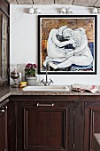 Küchenzeile mit Unterschrank aus dunklem Holz und Spülbecken mit Vintage Armatur, vor Wand mit modernem Gemälde