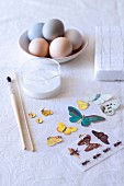 Craft utensils for decoupage Easter eggs: butterfly motifs, paintbrush and glass pot of glue