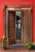 Brass floor lamp and planters flanking carved, wooden, half-opened double doors in Oriental style; view of planters on windowsill though doors