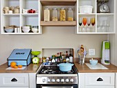 Blick auf Küchenzeile mit Küchenherd flankiert von Küchenarbeitsflächen, darüber offenes Regal zur griffbereiten Aufbewahrung von Geschirr & Küchenzubehör