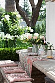 Set stone table and bench in antique French style with seat cushions and toile de jouy table runner: flowering garden in a background