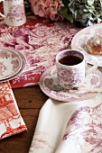 Geschirr und Tischwäsche mit rötlichen Toile-de-Jouy Mustern auf rustikalem Holztisch