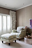 Armchair and matching footstool in corner next to terrace doors with closed interior shutters