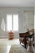 Orchid on shiny silver table next to brown armchair in front of elegant, glazed shower area